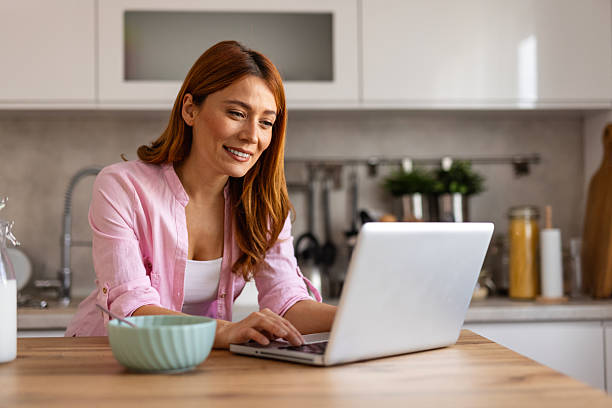 istock A young woman shops online from her kitchen, browsing her laptop while enjoying breakfast in a bright, modern space. 2211545189