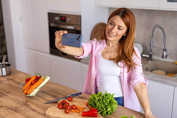 istock A woman in a modern kitchen prepares dinner while taking a selfie, capturing a fun and joyful moment. She is multitasking, cooking a delicious homemade meal while enjoying the process. 2211545244