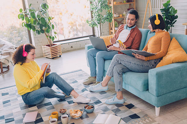 istock Young Friends Enjoying Quality Time Together at Home with Refreshments, Relaxing on Sofa and Floor with Tablets, Laptops, and Headphones 2211545526