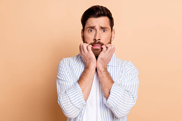 istock Young man showing a nervous gesture while biting his fingers against a beige background 2211548277