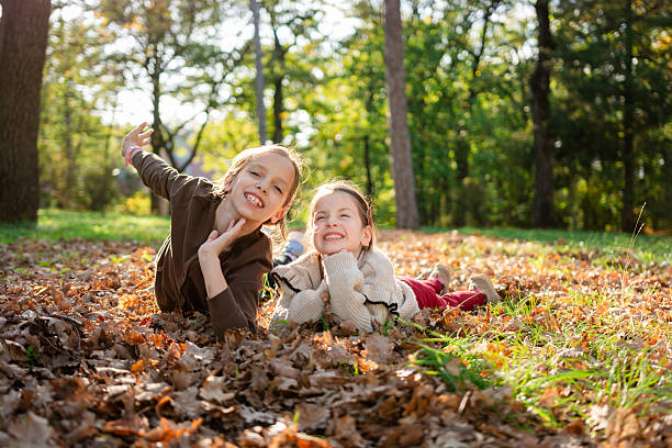 Two happy sisters enjoying a day in the park, lying on autumn leaves