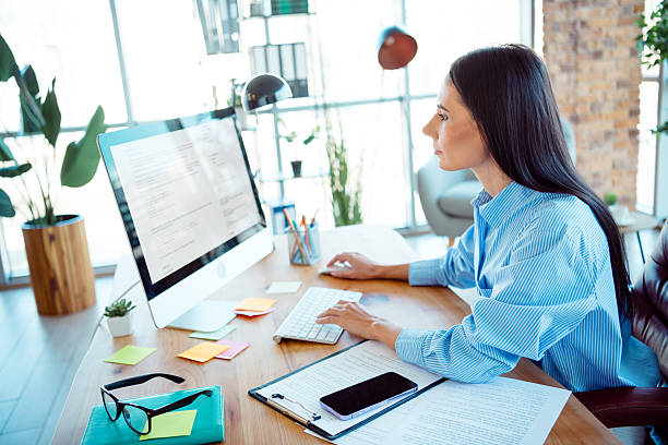 istock Young professional woman working in an office environment, viewing her screen attentively and staying focused, surrounded by modern decor 2211550963