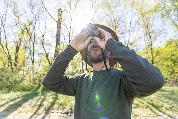istock Man with Binoculars Observing Birds in Sunlit Forest 2211551104