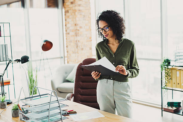 istock Young confident professional woman standing in a modern office workspace reading documents in natural daylight 2211552854