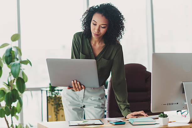 istock Confident young businesswoman using a laptop in a modern office space with natural light and greenery adding a lively ambience 2211552930