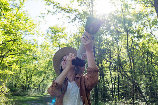 istock Woman Observing Nature Through Camera Lens in Sunlit Forest 2211557501