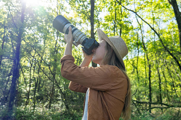 istock Woman Observing Nature Through Camera Lens in Sunlit Forest 2211557523