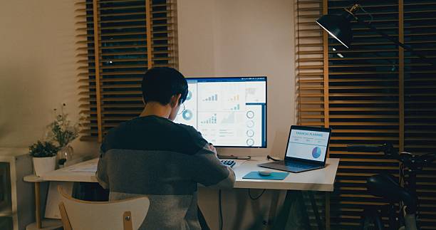 istock Young Asian man financial advisor working late at home, using a tablet and laptop, discussing strategy with clients via video call, showcasing remote work efficiency. Remotely and finance. 2211562053