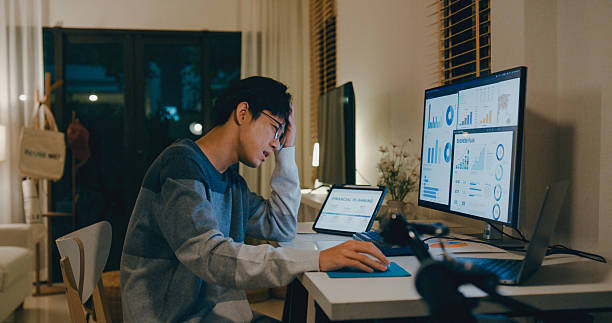 istock Young Asian man tired employee feeling mental burnout while working late at home office, overwhelmed by financial planning and data analysis tasks on multiple screens. Remotely and finance. 2211562080