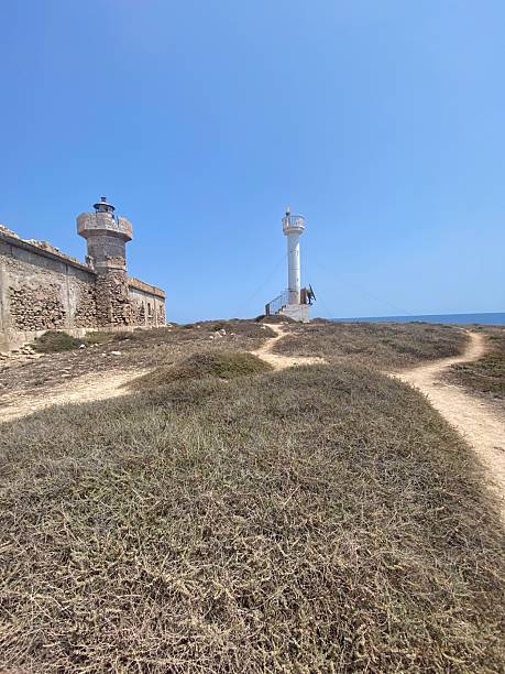 istock White lighthouse at Capo Passero towering above Mediterranean coastal landscape, serving as navigational landmark under bright azure sky 2211563228