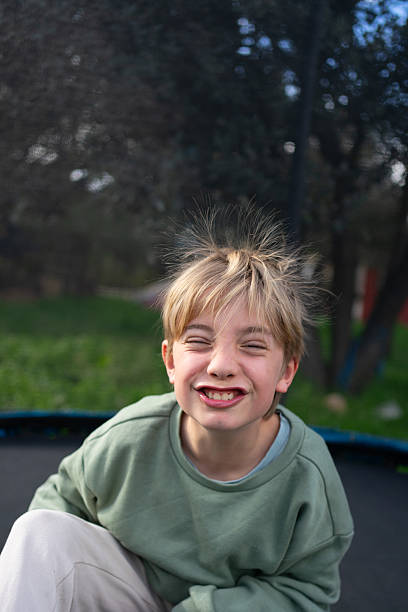 Blond child sitting on a trampoline with messy hair from static electricity, smiling and looking at camera