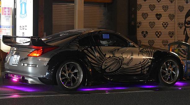 Tokio, Japan – April 12, 2023: A custom sports car with vibrant underglow lights parked on a city street at night, showcasing intricate side decals.