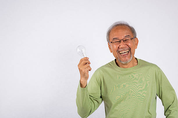 istock Portrait Asian old man is holding light bulb and smiling studio shot isolated on white background. Concept of intelligence and creativity, as the man is holding a symbol of innovation 2211566232