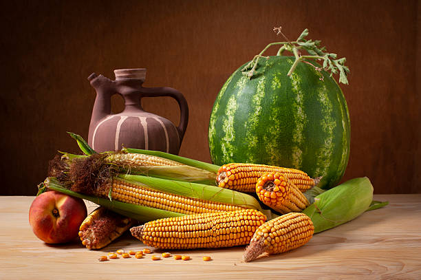 Still life, ceramic jug, watermelon, corn cobs, and fruit on a wooden table