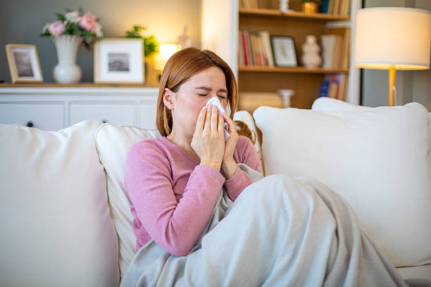istock Sick woman blowing her nose while sitting on the sofa 2211569037
