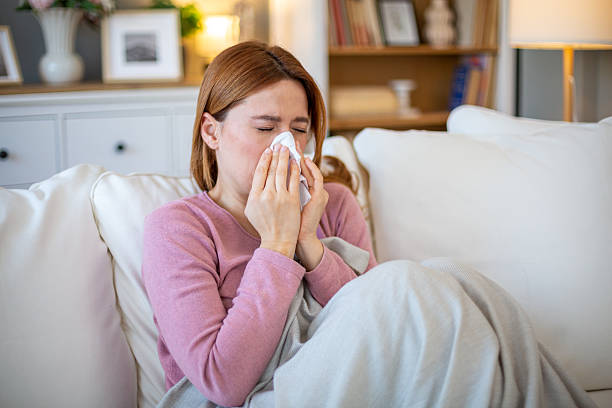 istock Sick young woman blowing her nose while sitting on sofa at home 2211569047