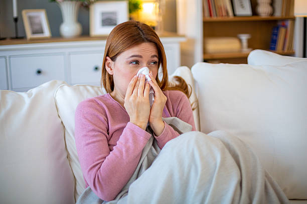 istock Sick young woman blowing her nose while sitting on sofa at home 2211569129