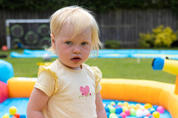 Young toddler looking at the camera while playing in an inflatable ball pit on a summers day outdoors in a garden in the North East of England.
