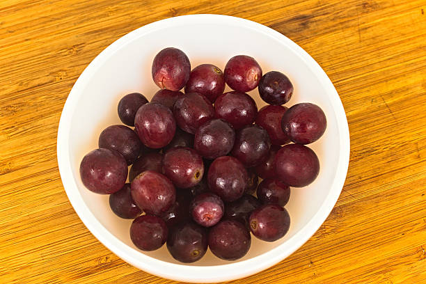 A close up shot of a white bowl filled to the brim with fresh, juicy red grapes, placed on a wooden surface.
