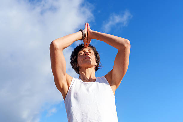 Mature woman practicing yoga outdoors with hands joined above head, eyes closed, and a serene expression