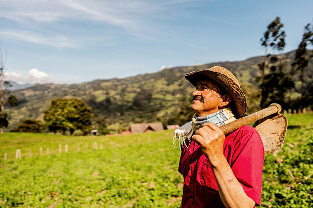 Farmer contemplating in a green field with a hoe resting on his shoulder