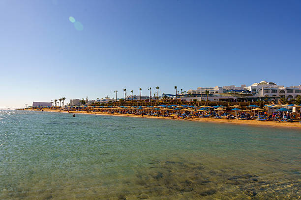 A beach with many umbrellas and people. The water is clear and the sky is blue