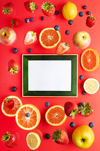 levitating blueberries, strawberries, apples and oranges on a red background. Photo frame for text. View from above.
