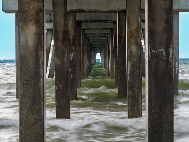 istock Weathered pier pillars  against swirling ocean waves. 2211599297