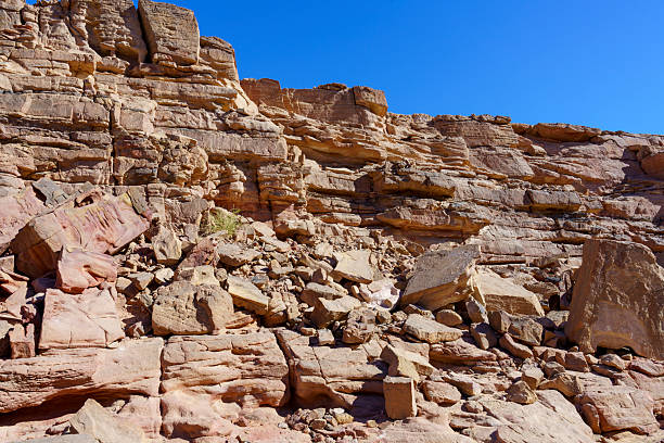 A rocky cliff with a blue sky in the background. The cliff is full of rocks and boulders, and the sky is clear and bright
