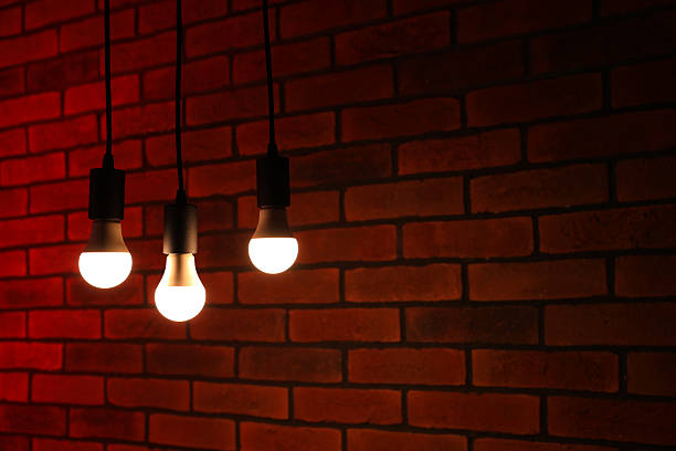 istock Glowing light bulbs hanging against brick wall, space for text 2211603936