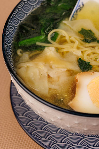 Hot ramen with egg and wonton in a bowl with blue ceramic spoon over wooden table