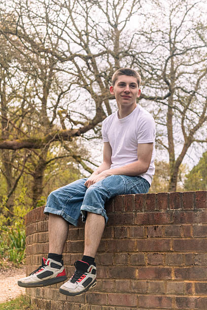 istock Teenage boy sitting on a brick wall 2211606852