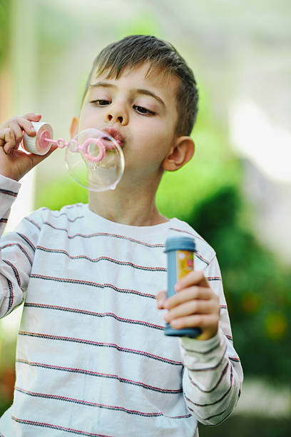 istock Little Boy Blowing Soap Bubbles Into Air Looking Focused 2211610242
