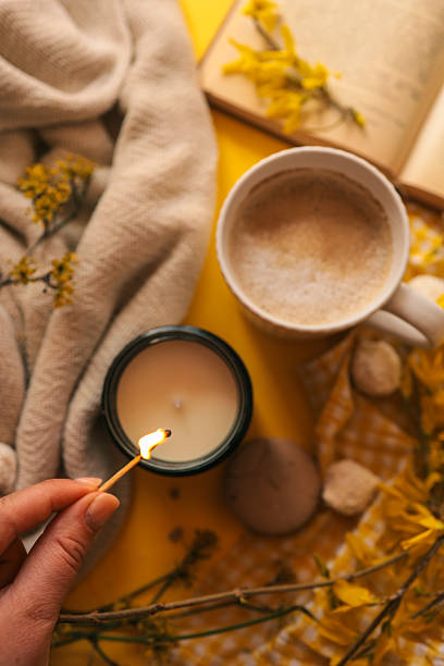 istock A cozy spring flat lay with a hand lighting a candle, a cup of coffee, a soft blanket, yellow flowers, an open book, and sweet treats on a bright yellow background, creating a peaceful mood 2211621185