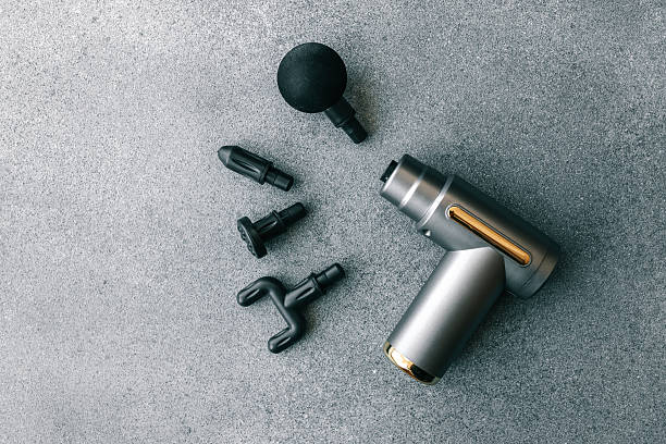 istock Modern massage gun with four interchangeable heads displayed on a grey textured surface, showcasing sleek design and multiple functionality options for muscle therapy 2211621273