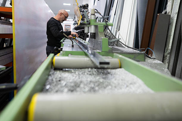 Carpenter measuring and cutting aluminum profiles using specialized machinery in a bustling workshop environment