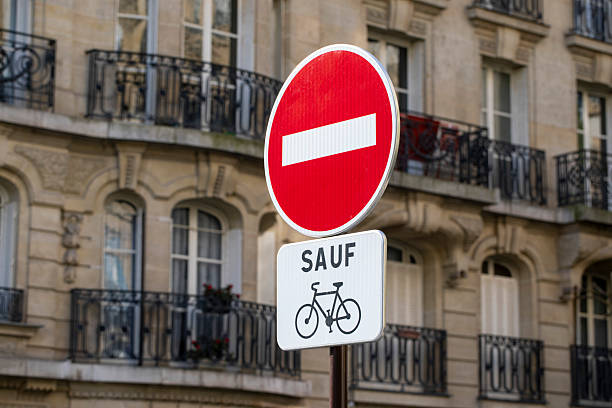 Front view of a street sign with a 'no' symbol and two opposite arrows against green corrugated metal wall