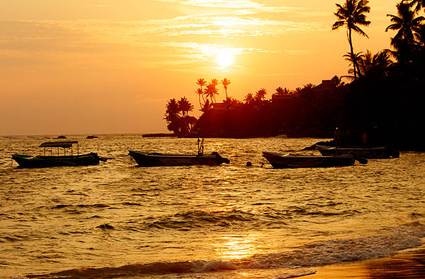 A sunset over the ocean with several boats in the water. The boats are small and are scattered throughout the water. The scene is peaceful and serene, with the sun setting in the background