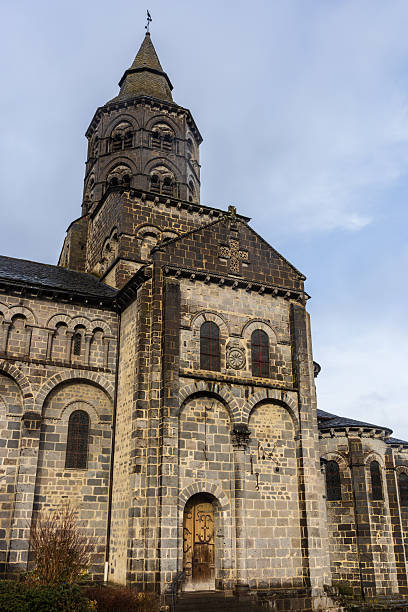 Basilica of Our Lady, medieval church. Orcival, Auvergne-Rhône-Alpes, France. Transept arm and bell tower of the Basilica of Our Lady of Orcival, medieval Romanesque church within the Parc des Volcans d'Auvergne. Orcival, Auvergne-Rhône-Alpes, France. orcival stock pictures, royalty-free photos & images