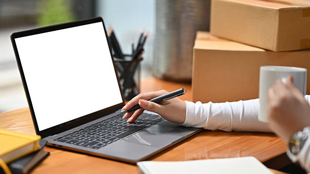 istock A close up of a hand holding a pen while using a laptop, surrounded by boxes, a notebook, and a cup, illustrating focus in a workspace setting, Small business set up concept 2211633057