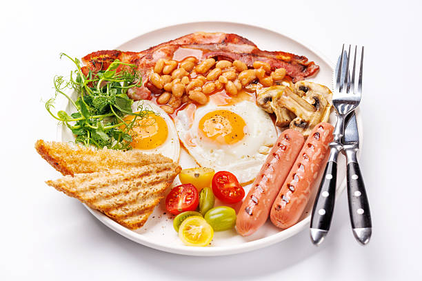 A classic breakfast plate featuring sunny-side-up eggs, crispy bacon, sausages, and fresh tomatoes for a hearty start to the day