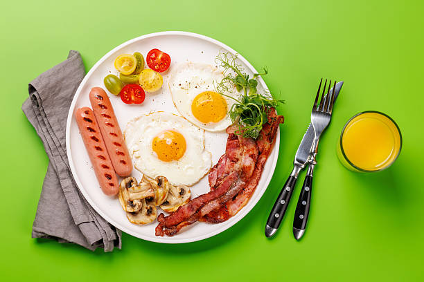 istock A classic breakfast plate featuring sunny-side-up eggs, crispy bacon, sausages, and fresh tomatoes 2211634171