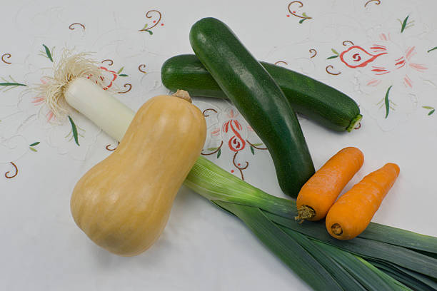 A leek, two zucchini, two carrots and a pumpkin on an embroidered tablecloth