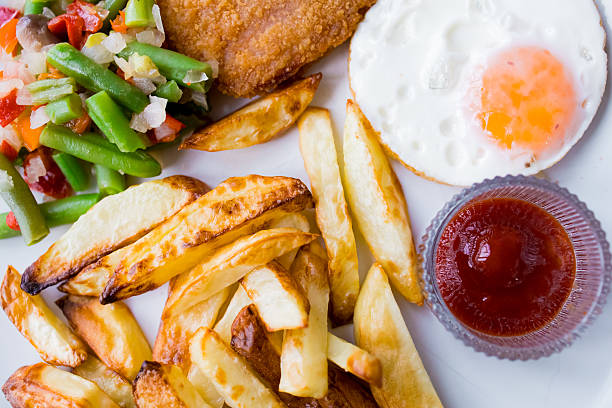 Crispy fries, breaded chicken, fried egg, green beans, and ketchup on white plate.