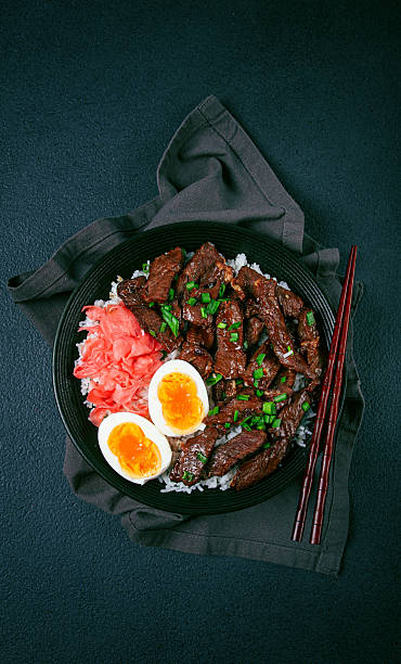 istock Udon Japanese beef with rice, pickled ginger, boiled egg slice, garnished with green onions, in a black bowl, with chopsticks, 2211641168