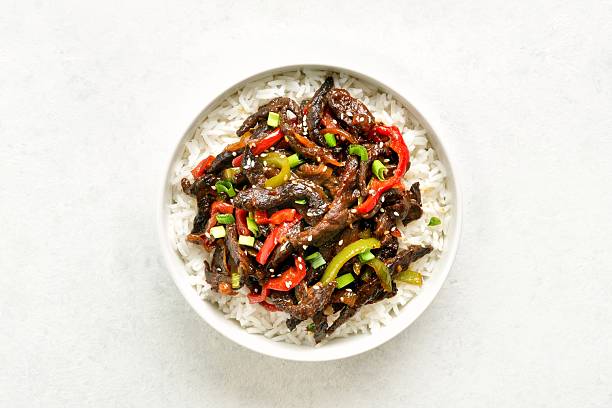 Crispy chilli beef in sweet and spicy chilli sauce served with basmati rice in bowl on light stone background. Top view, flay lay