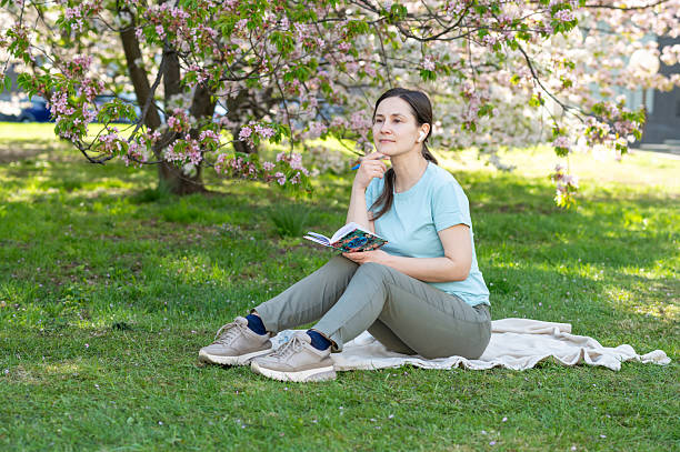 istock Young woman sitting on a blanket in a blooming spring park and writing notes in a notebook 2211644834
