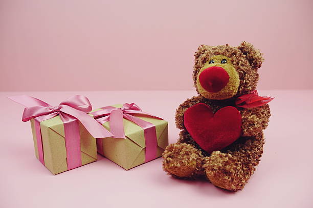 Smiling white teddy bear sitting at pastel pink wall and holding red soft heart. Empty place for emotional, sentimental text, quote or sayings on blank greeting card. Front view.