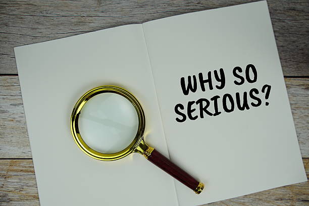 istock Why so Serious? text on notebook page with magnifying glass top view on wooden background 2211650078
