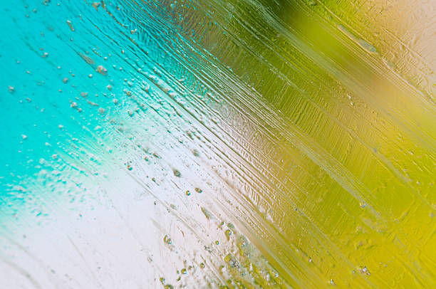 Bright water droplets rest on textured glass with vibrant blue and green hues seen in daylight.